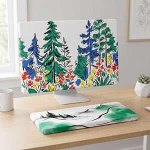 Op de afbeelding: Een computermonitorhoes en een bijpassende rechthoekige polssteun voor het toetsenbord. Beide items hebben een witte achtergrond met een kleurrijke bosillustratie van groene en blauwe dennenbomen, rode en gele bloemen en zwarte lijntekeningen.