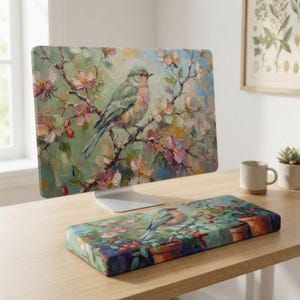 May include: A computer monitor and a rectangular wrist rest featuring an oil painting style print of a small bird perched on a flowering branch with soft pink and white blossoms against a muted green and blue background with visible brushstrokes.