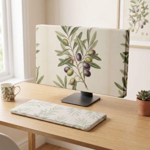 Puede incluir: Una funda para monitor de computadora y un reposamuñecas para teclado a juego con una ilustración botánica de ramas de olivo con aceitunas verdes y moradas sobre un fondo crema. El diseño muestra hojas y frutos detallados en la superficie.