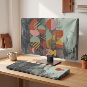 May include: A computer monitor cover and matching keyboard wrist rest featuring a dark gray and light green watercolor background with a central geometric pattern of circles, semicircles, and grids in shades of terracotta, mustard, and pink.