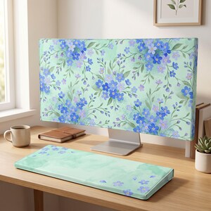 May include: A computer monitor cover and a matching rectangular keyboard wrist rest, both featuring a light mint green background with a repeating pattern of small blue and purple forget-me-not flowers and delicate green foliage.