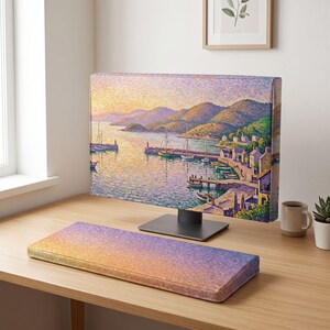 以下が含まれることがあります： コンピューターモニターカバーと、夕暮れ時の海岸沿いの港を描いた印象派風の絵画が施されたキーボード用リストレスト。帆船、なだらかな丘、小さな建物がオレンジ、紫、緑の色調で描かれています。