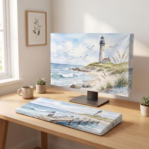 May include: A computer monitor cover and matching keyboard wrist rest featuring a watercolor coastal scene with a lighthouse, sandy dunes, tall beach grass, crashing ocean waves, and seagulls flying in a blue sky over a wooden pier.