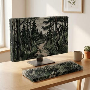 May include: A computer monitor cover and a matching rectangular keyboard wrist rest featuring a charcoal and green sketch of a winding forest path surrounded by tall pine trees. The artwork displays expressive, dark, hand-drawn lines.