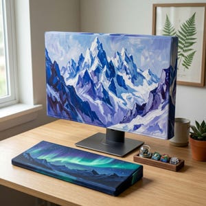 May include: A computer monitor cover featuring a painted mountain landscape in shades of blue and white, paired with a matching rectangular keyboard wrist rest displaying a vibrant green and purple aurora borealis night sky scene.