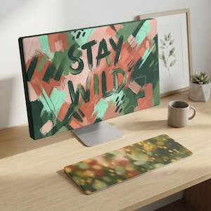 May include: A computer monitor displaying a digital artwork with the text STAY WILD in dark green brushstrokes over a background of abstract, overlapping rectangular shapes in shades of coral, sage green, mint, and dark forest green.