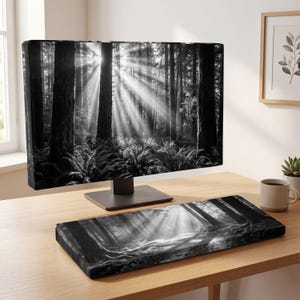 May include: A computer monitor and a rectangular keyboard wrist rest, both featuring a matching black and white photographic print of a dense forest with tall trees and sunbeams filtering through the canopy onto a bed of ferns.
