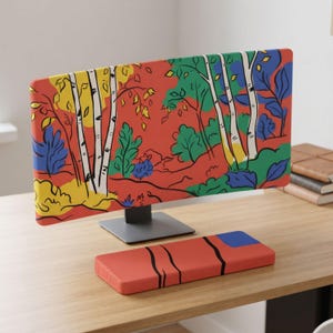 Puede incluir: Una funda para monitor de ordenador con una vibrante ilustración forestal estilizada que muestra abedules blancos, hojas amarillas y follaje verde y azul sobre un fondo naranja intenso, junto con un reposamuñecas rectangular a juego.