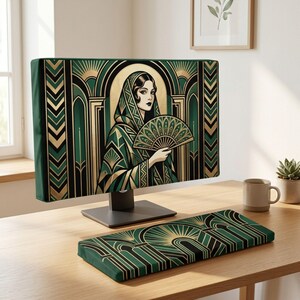 Op de afbeelding: Een computermonitorhoes en bijpassende toetsenbordpolssteun met een groen, zwart en goud geometrisch patroon. De monitorhoes toont een illustratie van een persoon met een kap die een decoratieve handwaaier vasthoudt.