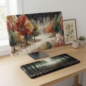 Könnte beinhalten: Ein Computermonitor mit einer herbstlichen Waldszene im Aquarellstil mit roten, orangefarbenen und grünen Bäumen, kombiniert mit einer passenden rechteckigen Schreibtischunterlage, die einen dunklen, nebligen Waldweg zeigt.