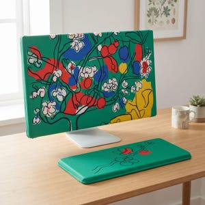 May include: A green computer monitor cover and a matching rectangular keyboard wrist rest. Both items feature a vibrant, abstract botanical print with black line art of branches, white flowers, and solid shapes in red, blue, and yellow colors.