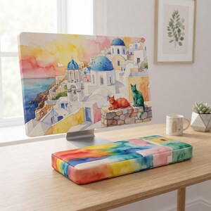 Peut inclure: Un écran d'ordinateur affichant une aquarelle d'un village côtier grec avec des bâtiments aux dômes bleus, un chat orange et un chat vert assis sur un mur en pierre. Un repose-poignet rectangulaire assorti présente un lavis aquarelle abstrait.