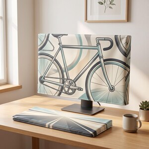 Op de afbeelding: Een computermonitorhoes met een lichtblauwe fietsillustratie op een crèmekleurige achtergrond met cirkelvormige patronen, gecombineerd met een bijpassende rechthoekige polssteun voor het toetsenbord met een geometrisch wegontwerp in blauwtinten.