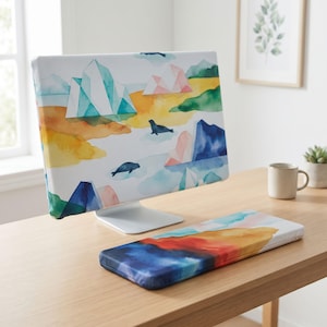 Pode incluir: Uma capa para monitor de computador e um apoio de pulso para teclado a condizer com uma impressão em aguarela de icebergs, focas e paisagens abstratas em tons de azul, verde, amarelo e rosa sobre um fundo branco, colocados numa secretária de madeira.