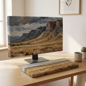 May include: A computer monitor and a rectangular wrist rest featuring an oil painting style landscape of desert cliffs under a dark, cloudy sky. The artwork displays textured brushstrokes in shades of tan, brown, gray, and deep blue across both items.