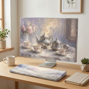 May include: A computer monitor displaying a digital painting of a silver tea set on a lace tablecloth with steaming cups and a vase of flowers. The monitor sits on a wooden desk with a matching keyboard wrist rest, a white mug, and a notebook.