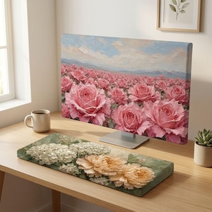 May include: A computer monitor displaying a digital painting of a vast field of pink roses under a pale blue sky, paired with a matching rectangular keyboard wrist rest featuring a floral design of white and peach-colored blossoms on a green base.
