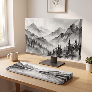 May include: A computer monitor cover and a matching keyboard wrist rest featuring a black and white watercolor landscape print of mountain peaks and pine trees. The design displays a misty, layered mountain range with dense forest silhouettes.
