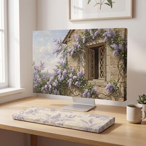 May include: A computer monitor displaying a painting of a stone cottage wall with an open lattice window surrounded by blooming purple lilac flowers, accompanied by a rectangular keyboard wrist rest featuring a matching purple floral pattern.