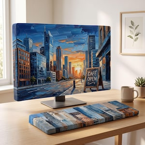May include: A computer monitor and a matching keyboard wrist rest featuring an oil painting style cityscape at sunset with tall buildings, a street, and a sidewalk chalkboard sign that reads CAFE OPEN in white text on a wooden frame.