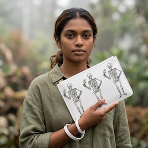 May include: A white rectangular zipped pouch featuring a black line art illustration of three skeletons, each holding a small green flower. The pouch includes a matching white wrist strap attached to the side, providing a functional carrying option.