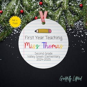 May include: A round white ornament with a lined paper pattern, a yellow pencil graphic, and black text reading First Year Teaching, Miss Thomas, Second Grade, Valley Green Elementary, 2024-2025. The ornament features a red ribbon for hanging.