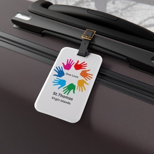 May include: White luggage tag with a colorful handprint design and the text "One Love" and "St. Thomas Virgin Islands".