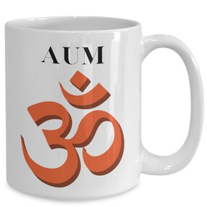 May include: White ceramic mug with a large orange Om symbol and the word "AUM" in black. The mug has a curved handle and a glossy finish, suitable for hot or cold beverages.