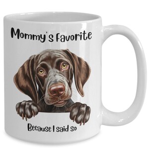 May include: White ceramic coffee mug with a brown and white German Shorthaired Pointer dog peeking over the rim. The mug has the text "Mommy's Favorite Because I said so" printed on it.