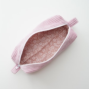 Könnte beinhalten: Hellrosa Stifteetui aus Cord mit weißem Reißverschluss und floral gemustertem Innenfutter. Das rechteckige Etui hat an einem Ende eine kleine Stoffschlaufe. Das Etui ist geöffnet und zeigt das florale Futter.