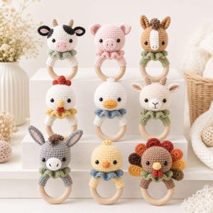 May include: A collection of nine handmade crochet animal teethers. Each teether features a different farm animal head, including a cow, pig, horse, chicken, duck, goat, donkey, chick, and turkey, attached to a wooden ring. The animals are in various colors.