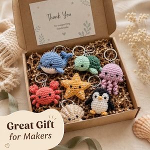 May include: A cardboard gift box containing six crocheted keychains shaped like a blue whale, green turtle, pink jellyfish, red crab, yellow starfish, beige seashell, and a black and white penguin. A card inside reads Thank You for supporting handmade.