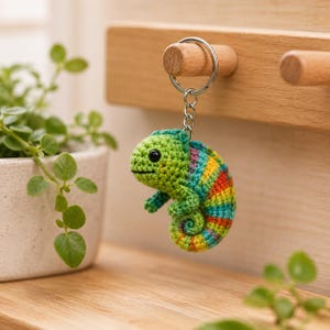 May include: A crocheted chameleon keychain featuring a green head and body with a multi-colored striped tail in shades of yellow, orange, blue, and purple. The small stuffed figure is attached to a silver-toned metal split ring and chain.