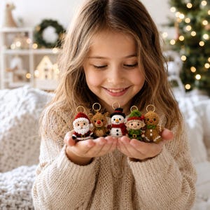 May include: A set of five small crocheted Christmas ornaments featuring a Santa Claus, a reindeer, a snowman, an elf, and a gingerbread person. Each figure is crafted with yarn in festive colors and includes a gold-toned metal ring for hanging.