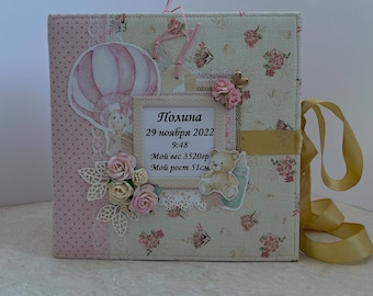 May include: A pink and white scrapbook with a floral pattern and a hot air balloon design. The scrapbook has a gold ribbon and a tag that says "Polina 29 ноября 2022 9:48 Мой вес 3520гр Мой рост 51см"