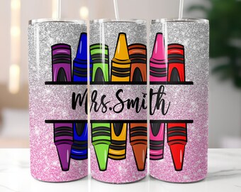 Puede incluir: Un vaso brillante con un fondo rosa y plateado. El diseño presenta crayones coloridos encima y debajo de una pancarta negra con el nombre "Mrs. Smith" en escritura negra. El vaso tiene una pajita.