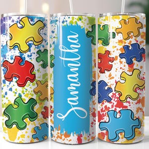May include: Three stainless steel tumblers with a white background and colorful puzzle pieces. The middle tumbler has the name Samantha written in blue on a blue background.