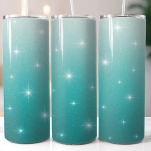 May include: Three glittery, ombre tumblers with a teal to light blue gradient. Each tumbler has a straw and is decorated with sparkling starbursts. The tumblers are cylindrical and appear to be made of stainless steel.
