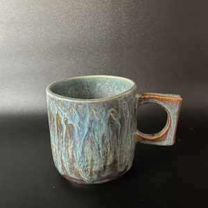 May include: A blue and brown ceramic mug with a unique glaze pattern. The mug has a square-shaped handle.