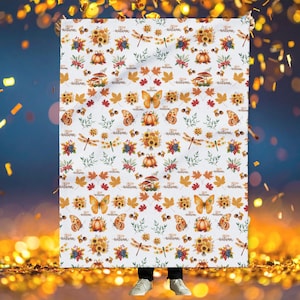 Può includere: Coperta bianca con un motivo ripetuto di illustrazioni a tema autunnale. Il design include girasoli, zucche, farfalle, foglie e il testo "Hello Autumn". Un accogliente elemento d'arredo per la casa a tema autunnale.