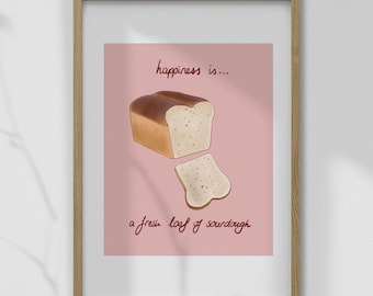 May include: A framed print featuring a loaf of sourdough bread with a slice cut out, set against a pink background. The text reads "happiness is... a fresh loaf of sourdough" in a handwritten style. The frame is made of wood.