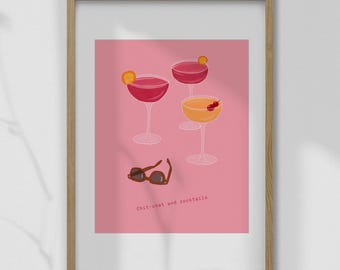 May include: A framed print featuring three cocktail glasses with pink and yellow drinks, garnished with orange slices and cherries. Brown sunglasses rest below the glasses. The text "Chit-chat and cocktails" is at the bottom.