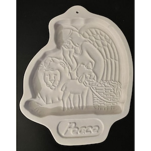 Puede incluir: Adorno de pared de cerámica blanca con un relieve de un ángel, un león, un cordero y una cesta. La palabra "Peace" está grabada en la parte inferior. Tiene un agujero en la parte superior para colgar.