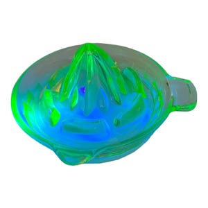 May include: A clear glass citrus juicer with a vibrant green reamer and a blue-green bowl. The juicer has a handle and a spout for easy pouring. The design is modern and functional, perfect for making fresh juice.