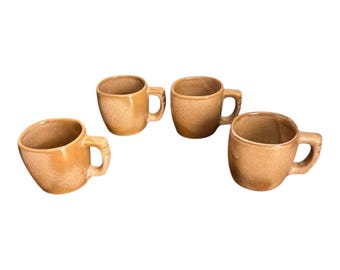 Pode incluir: Quatro canecas de cerâmica com um esmalte texturizado, salpicado e bege. Cada caneca tem um corpo arredondado, uma alça e uma forma ligeiramente irregular, sugerindo qualidade artesanal. As canecas estão dispostas sobre um fundo branco.