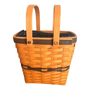 May include: A brown wicker basket with two black handles. The basket has a black trim around the top and a black stripe around the middle.