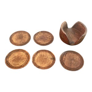May include: A set of six wooden coasters with a holder. The coasters are oval-shaped with carved floral designs and a distressed finish. The holder is a curved, open-top design, also made of wood.