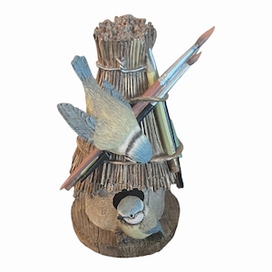 Könnte beinhalten: Eine dekorative Vogelhaus-Skulptur mit zwei Blaumeisen. Das Vogelhaus besteht aus Stroh und Holz, mit Bleistiften und Pinseln. Die Skulptur hat eine rustikale, natürliche Ästhetik mit detaillierten Texturen und realistischen Vogelfiguren.