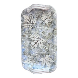 Puede incluir: Bandeja rectangular de cerámica con una combinación de colores azul claro, gris y blanco. La bandeja presenta un diseño de hojas con hojas blancas y vetas marrones. Tiene dos asas curvas.