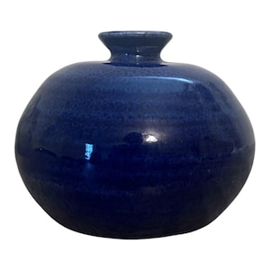 May include: A round, dark blue ceramic vase with a small, cylindrical neck. The vase has a glossy finish and a textured surface. The overall shape is spherical, with a slightly flattened base. The vase is suitable for home decor.